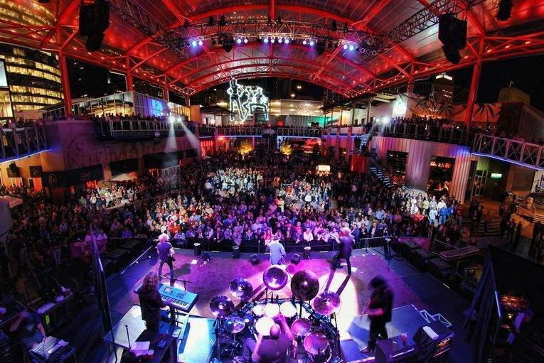 A rock band plays a concert at the Power and Light District before a large crowd that spans two levels.
