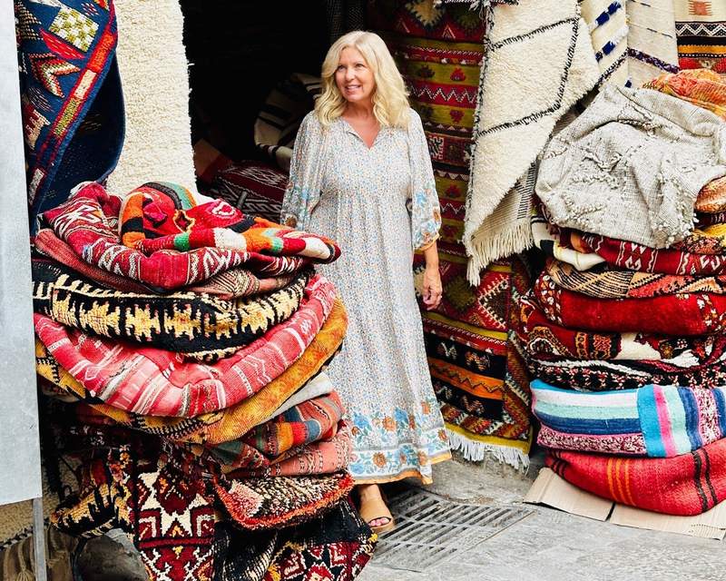 A woman walking through the Marrakech Medina surrounded by colorful rugs.