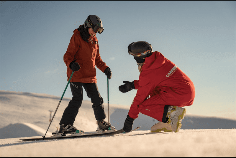 Ski instructor teaching a new skier how to snowplow.