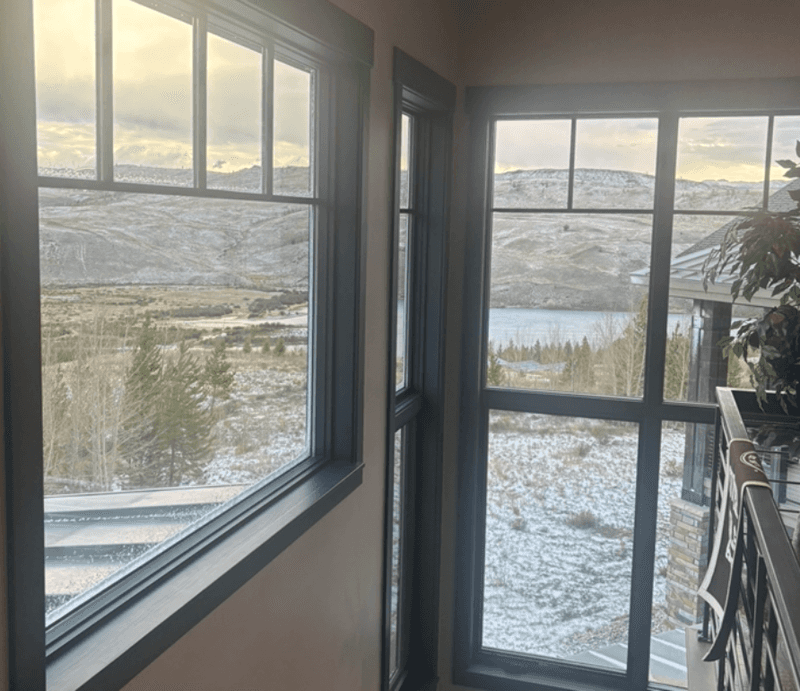 View through large windows showing a snowy valley rolling hills and distant water outside a lodge.