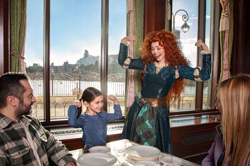 A young girl and her parents enjoy a meal with Princess Merida from Disney and Pixars Brave. The girl is grinning and posing with Princess Merida.