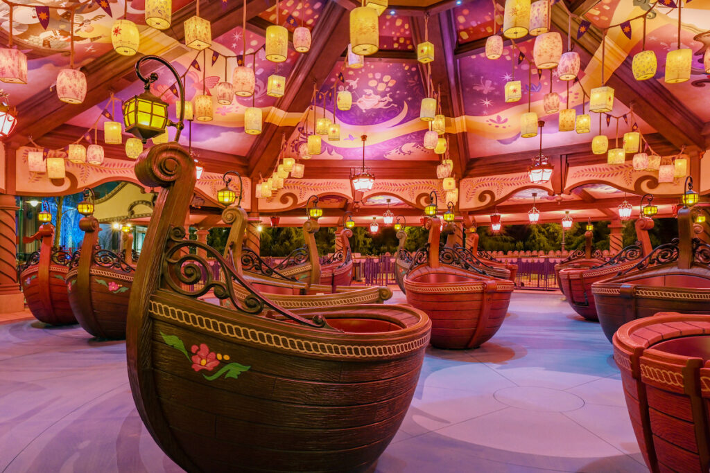 Ornate wooden gondolas are pictured beneath a brightly painted purple orange and yellow ceiling and lit by lanterns designed to look as if theyre floating. This a look at the new family friendly ride Raiponce Tangled Spin at Disneyland Paris.