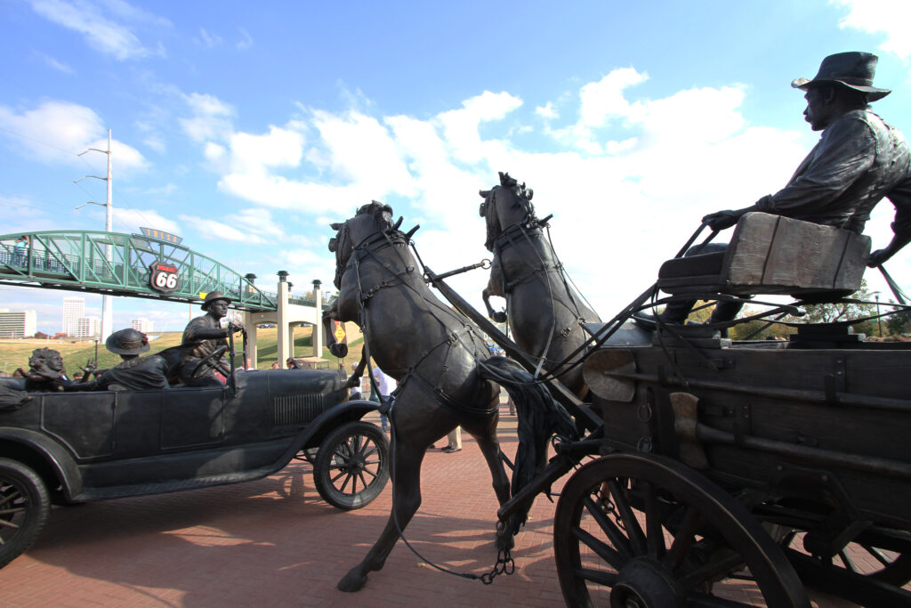East Meets West statue in Tulsa with the Route 66 pedestrian bridge in the background.