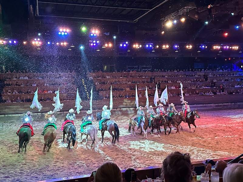 Ten horses and riders with flags in a stadium.