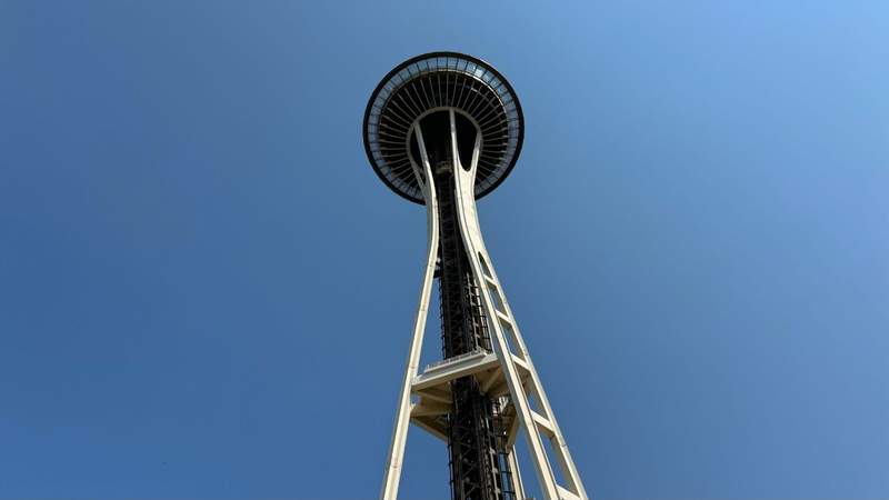 blue sky with tall white skinny building and black circular floor at the top of the Space Needle in Seattle