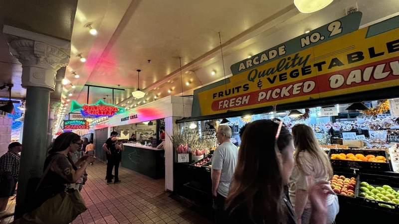 yellow sign with quality fruits and vegetables written and people walking on tile at Pike Place Market in Seattle