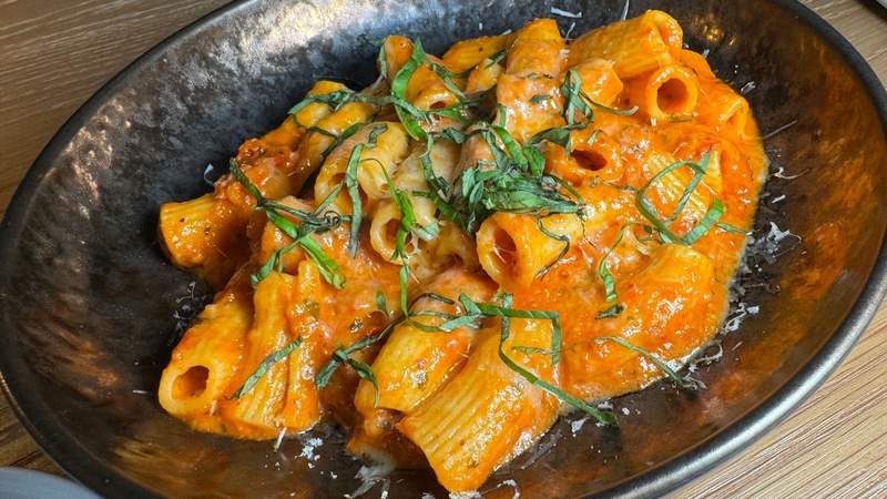 Black bowl filled with rigatoni pasta and orange sauce and green parsley at La Loba in Seattle.