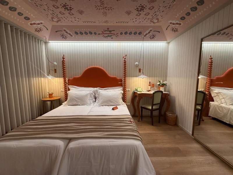 A double bed with a bright orange headboard sits in a bright room with a colorful ceiling.