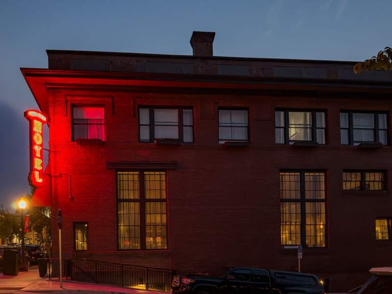 Brick facade and neon hotel light glowing red and windows lit from within.