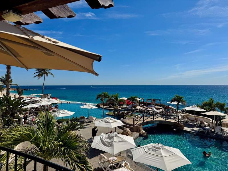 White pool umbrellas by a pool overlooking the turquoise ocean beyond at Hacienda del Mar Los Cabos