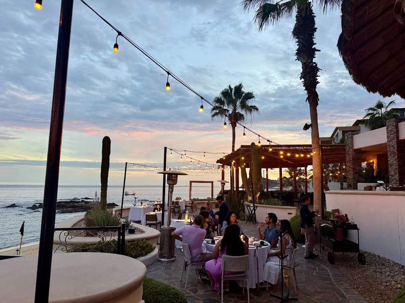 Diners sit at a round table with a view of the ocean at sunset
