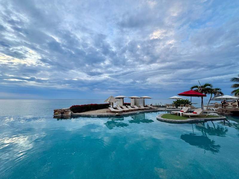 An infimity pool overlooking the ocean, with loungers and a red umbrella