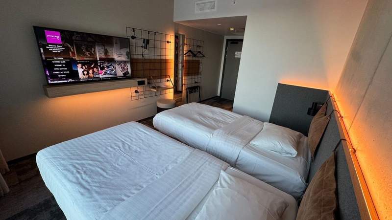 Two twin beds sitting inside of a beige room featuring a flat screen televsion. 