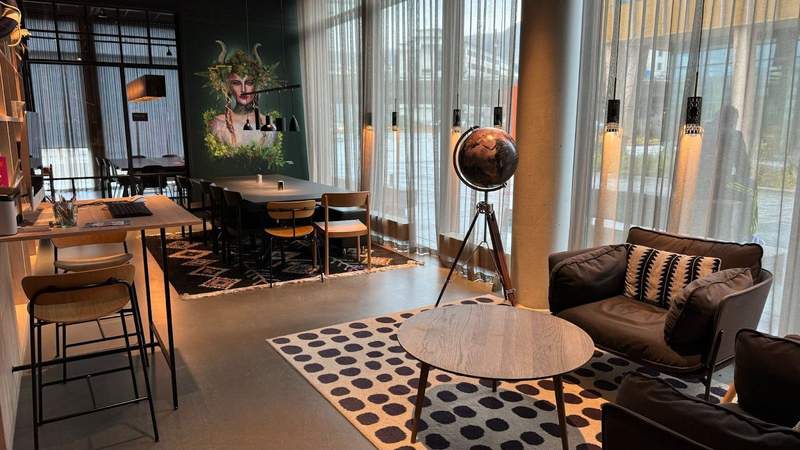 A room with a table and chairs a desk with a computer black cushion chairs on top of a rug next to an illustration and a globe. 