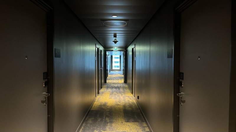 A grey corridor containing two adjacent side of hotel rooms with a yellow green and gray carpet. 