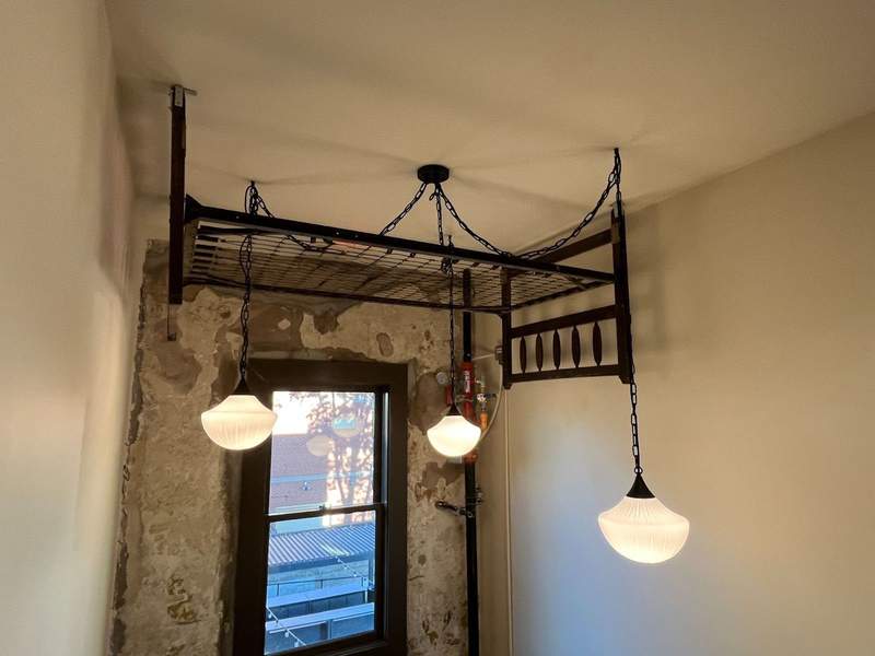 An upside down metal bedframe hangs from the ceiling surrounded by three hanging lamps.