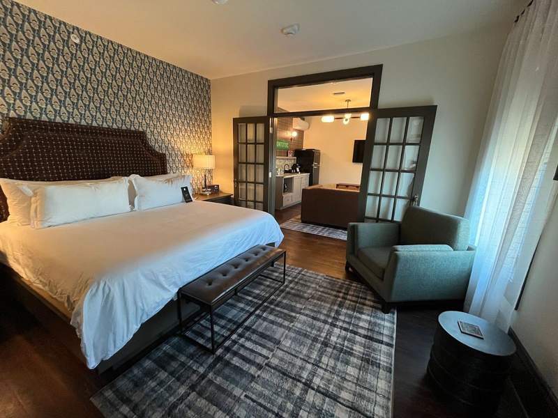 A hotel suite with a bed easy chair and glass doors leading to a sitting area. 