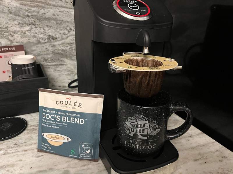 A coffee maker ready to brew with a Hotel Pontotoc mug under the filter. 