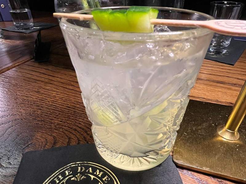 Cocktail in a glass tumbler with a cucumber garnish.