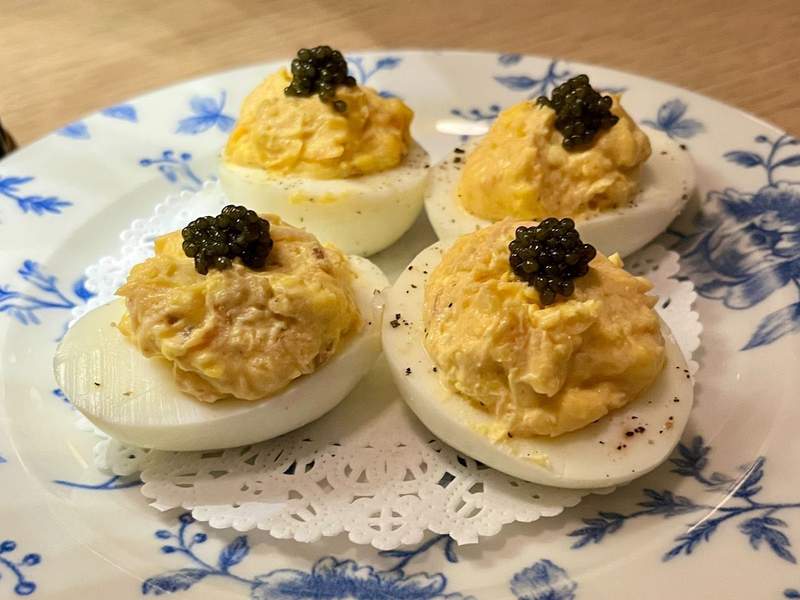 A blue and white porcelain plate holds hold four deviled eggs topped with caviar. 