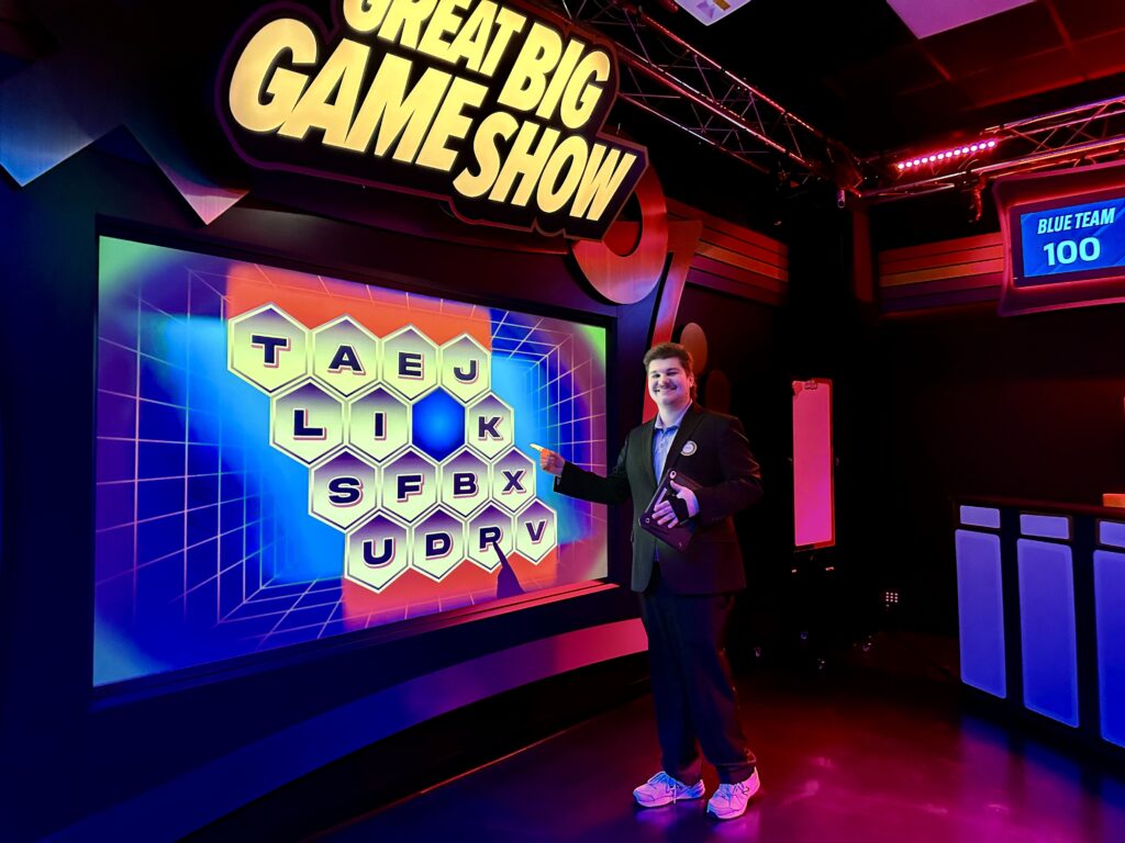 Game show host in front of letter board on Great Big Game Show set in Times Square.