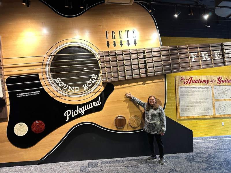 A lady in front of a huge guitar.