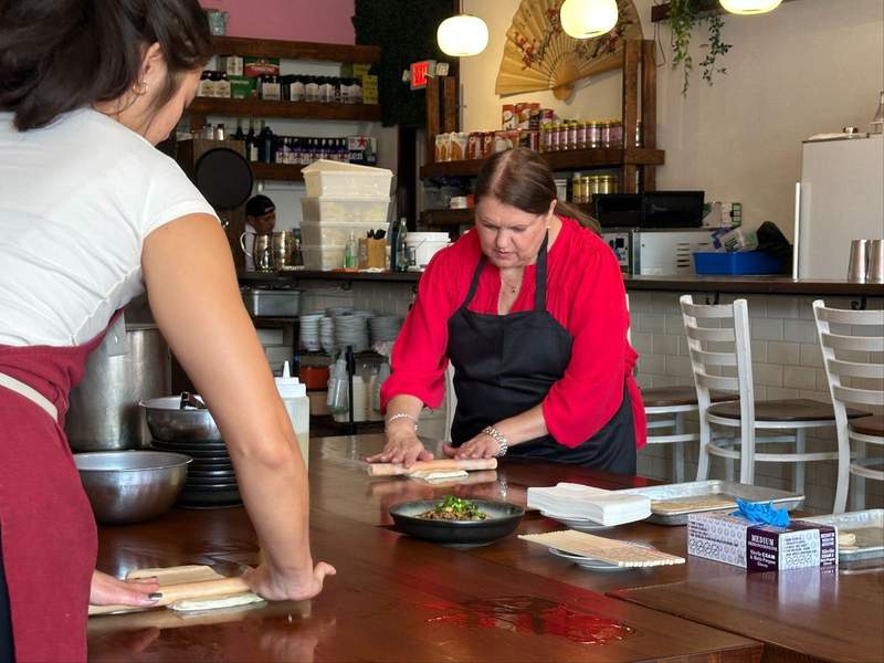 Two women rolling dough on a counter. 