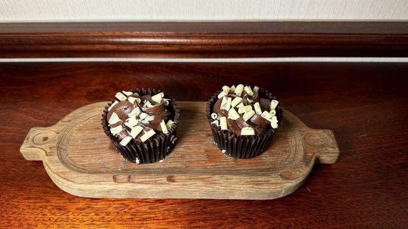 Two chocolate cupcakes on a wood serving tray on a table in a suite at The Stafford London. 