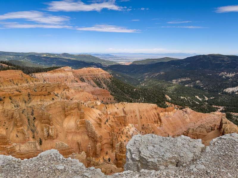 View of layered red rocks amphitheater tree covered mountains and a valley in the distance.