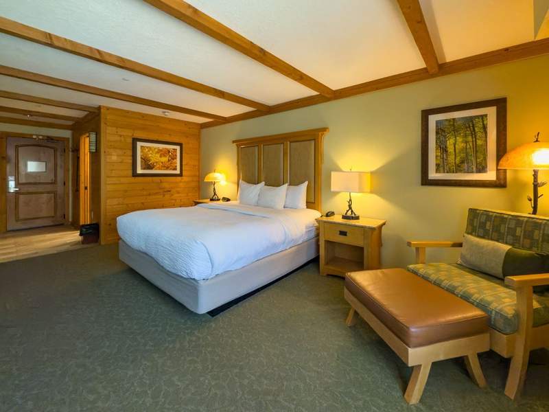 Hotel room with king bed an easy chair and ottoman and lights that make it warm and cozy.