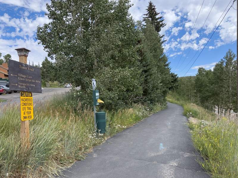 A paved trail bordered with trees and signage under a blue and cloudy sky.