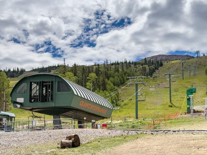 A chairlift structure and chairs moving up the mountain under a partly cloudy deep blue sky.