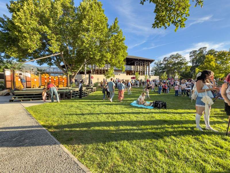 People gathered on the green laws with trees and a theater in the background.