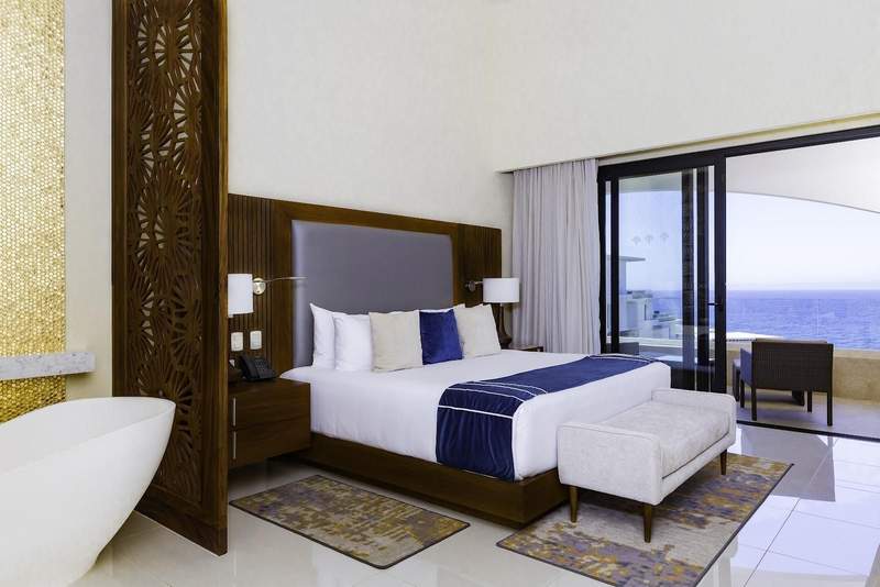 A single hotel bed with a balcony and ocean view in the background.