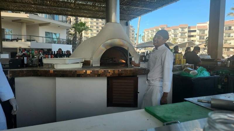 Man standing next to a wood burning pizza oven.