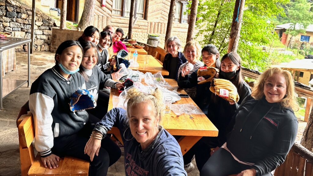 A group of women of all ages seated around a large wooden table and smiling at the camera in Bhutan.