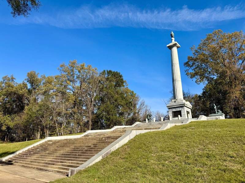 A tall white monument on a grassy hill