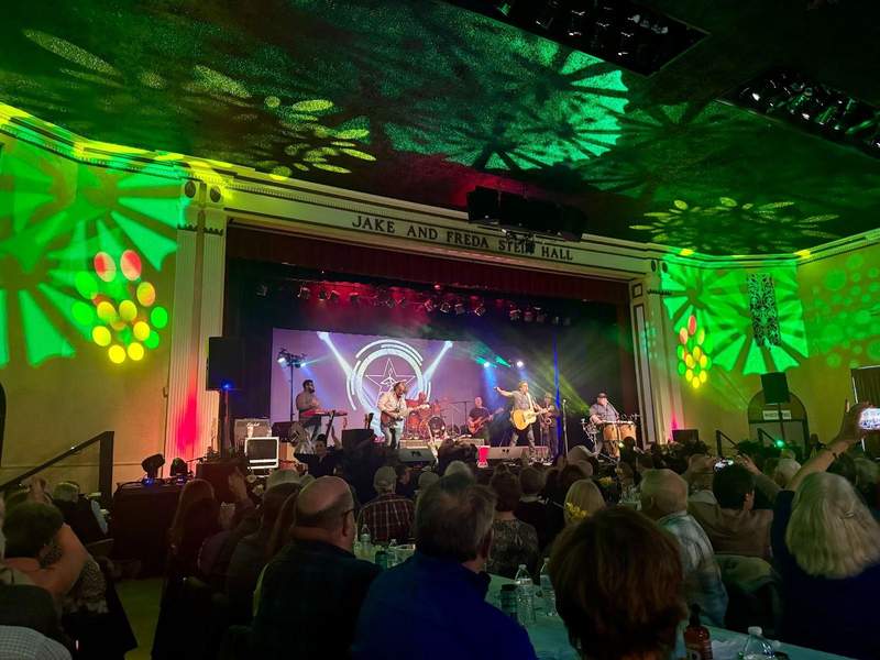 Musicians on a stage play for a large crowd in a school auditorium