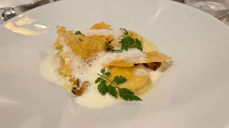 white plate with a center filled with ravioli and baked cheese next to shreds of green basil from The Shelbourne