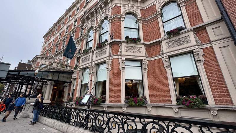 Tall brick building with large windows next to a navy blue flag and a black awning outside of The Shelbourne in Dublin.