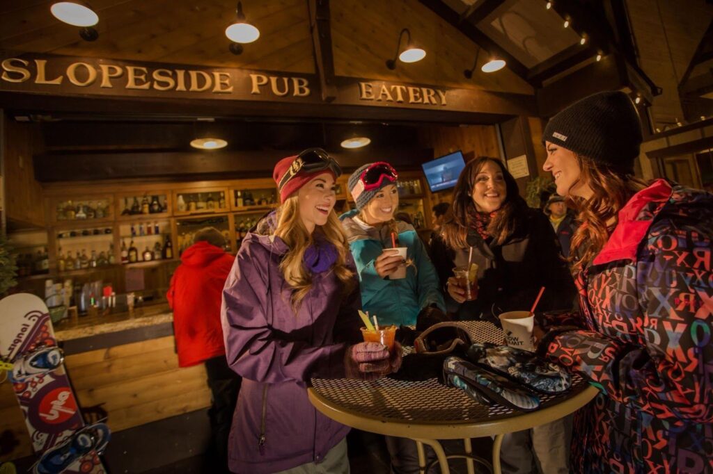 Four women in winter ski gear sipping cocktails at a cozy pub on Big Bear Mountain.