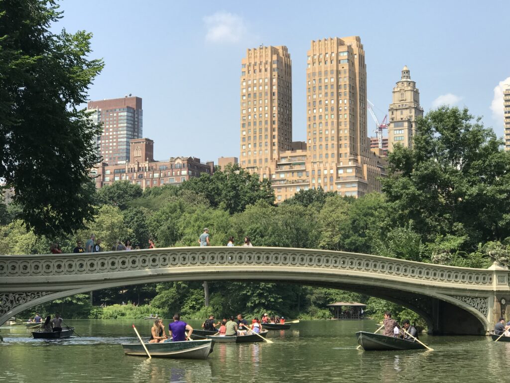Rowboats on the lake in NYC's Central Park with West Side apartment buildings in the background.