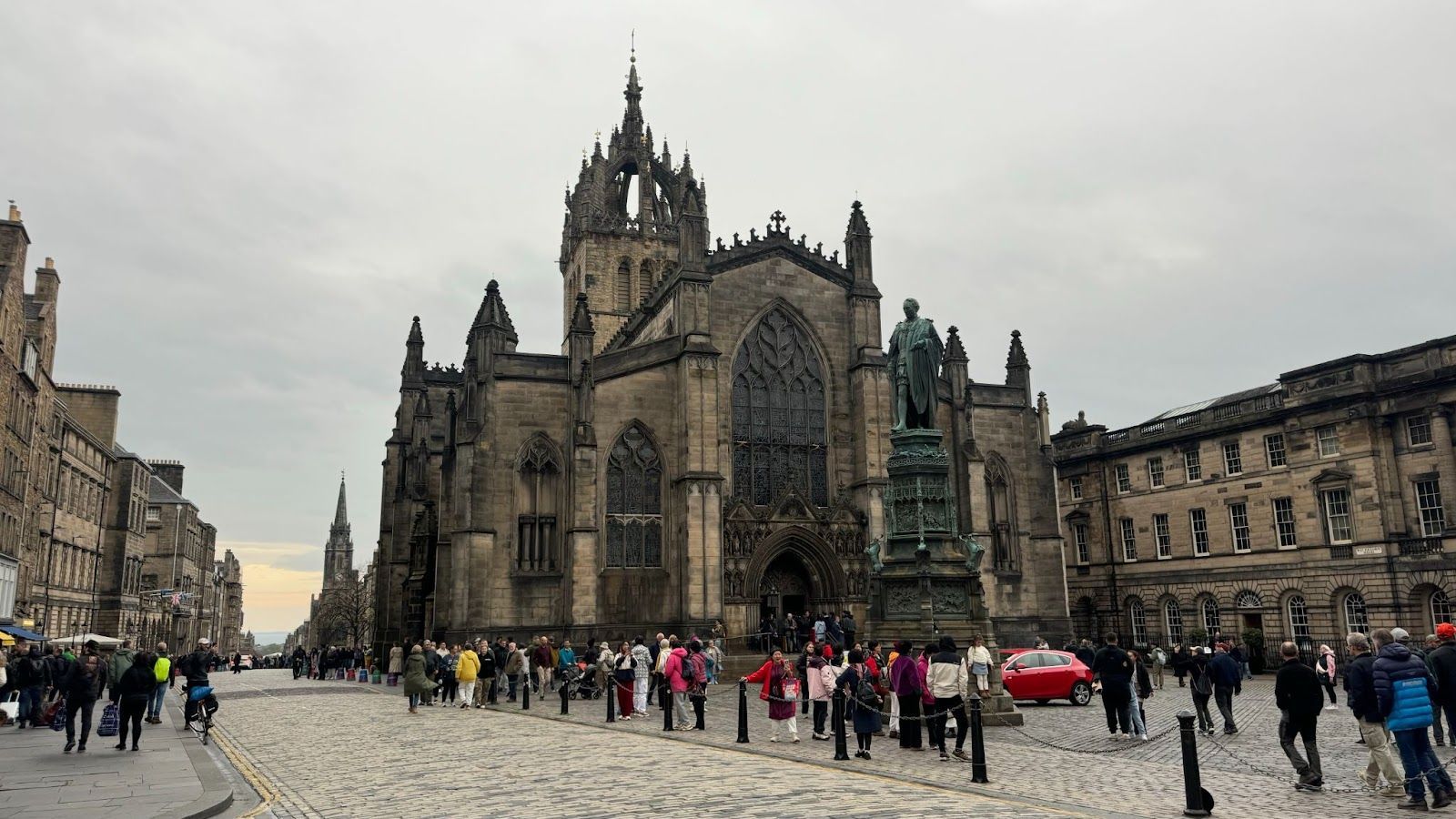 Old gothic cathedral with pointed spires with people walking on the cobblestone in Edinburgh 