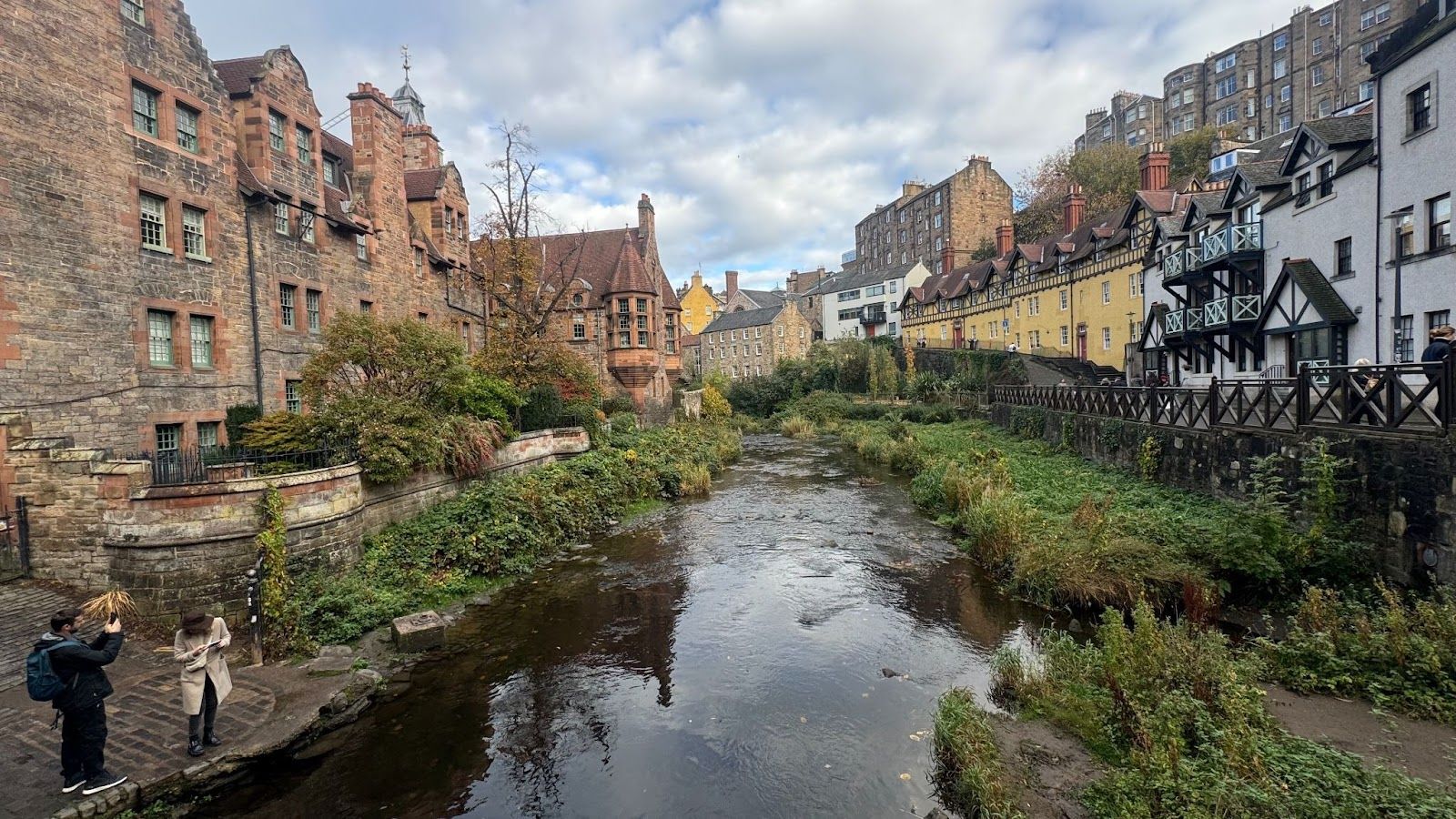 colorful cottages lined up on the sides of a river flowing through next to green grass in Deans Village in Edinburgh