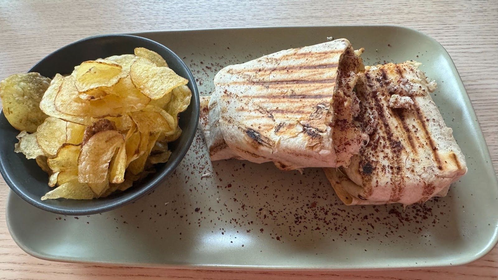 green plate with a black bowl of potato chips next to a chicken wrap sliced in half at Comb in Edinburgh.