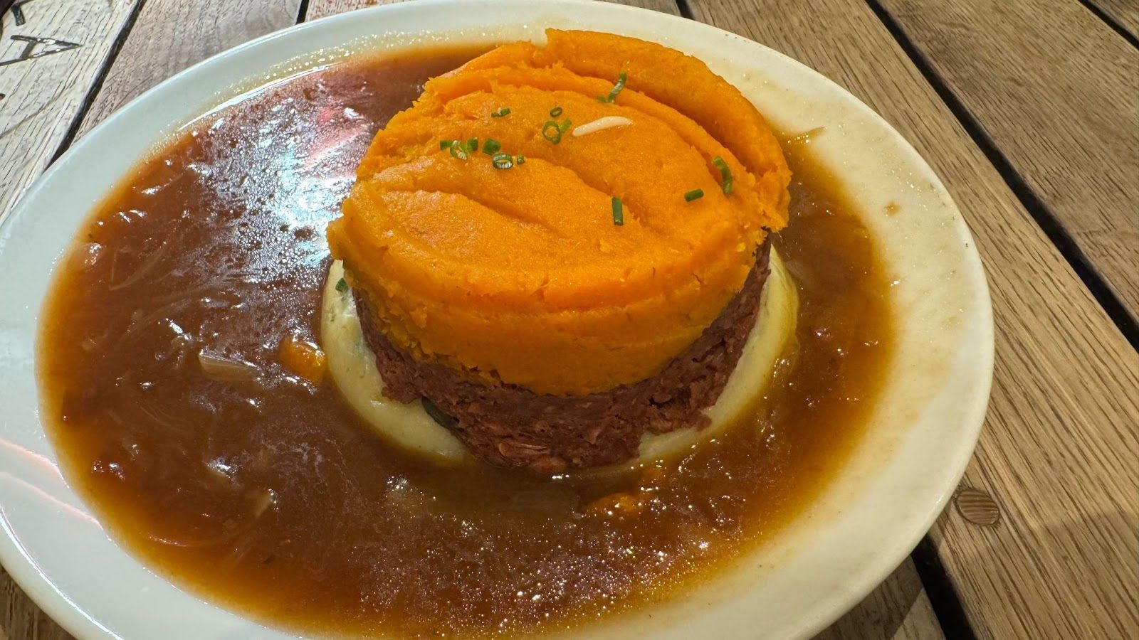 Large white plate with brown onion gravy on the rim and a center stack of potatoes and brown lentils from Makars Mash Bar in Edinburgh