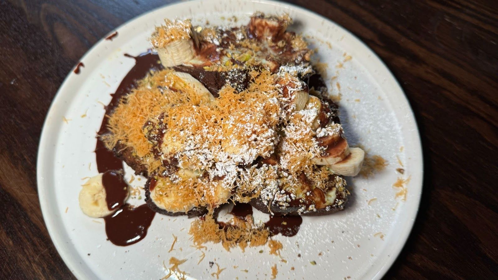 White plate with pieces of banana bread topped with slices of banana chocolate sauce and toasted almonds at Greenwoods in Edinburgh