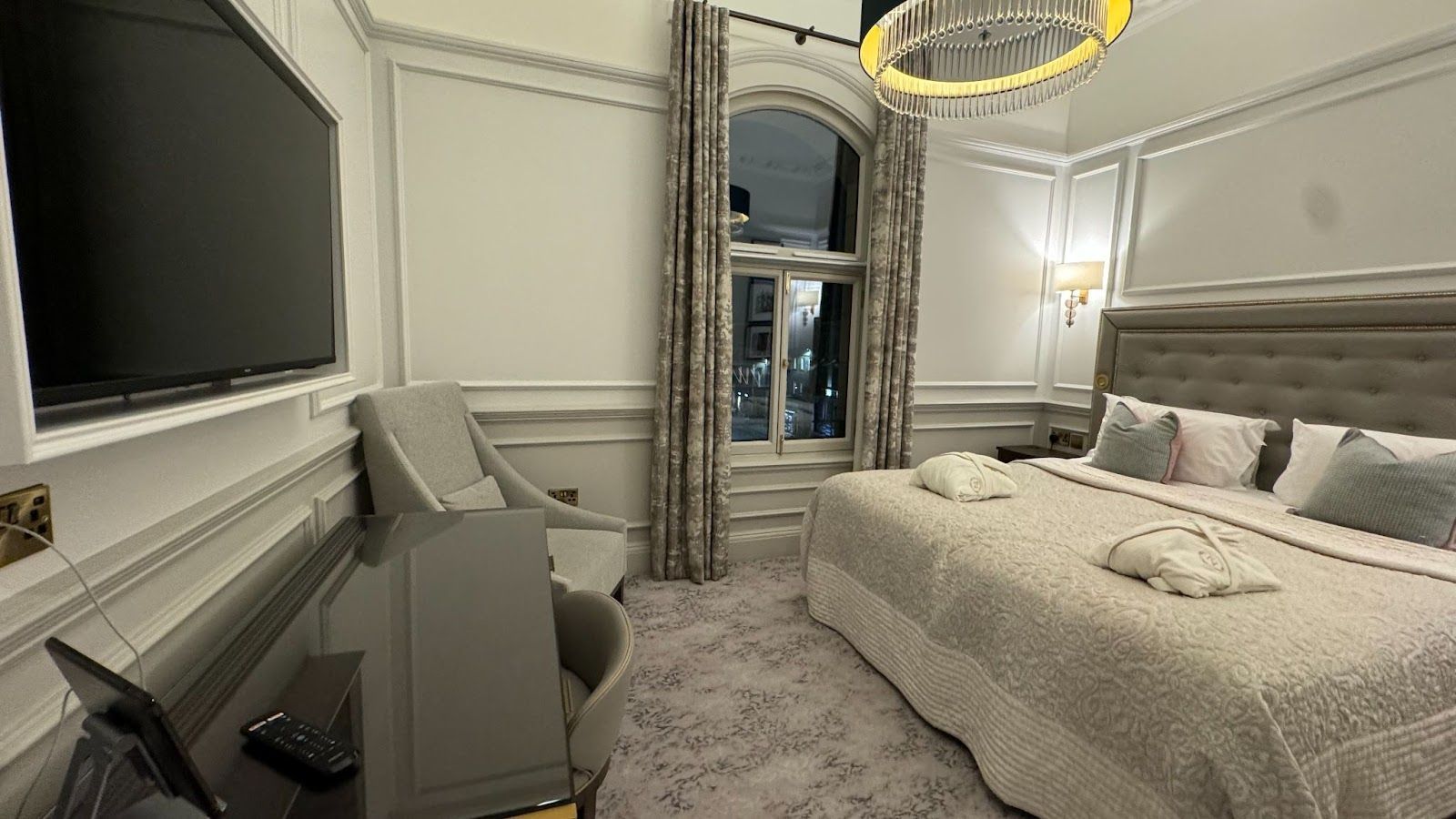 large bed with robes in front of a grey headboard across from a black desk with a remote and a flat screen television at Righ Residences in Edinburgh.