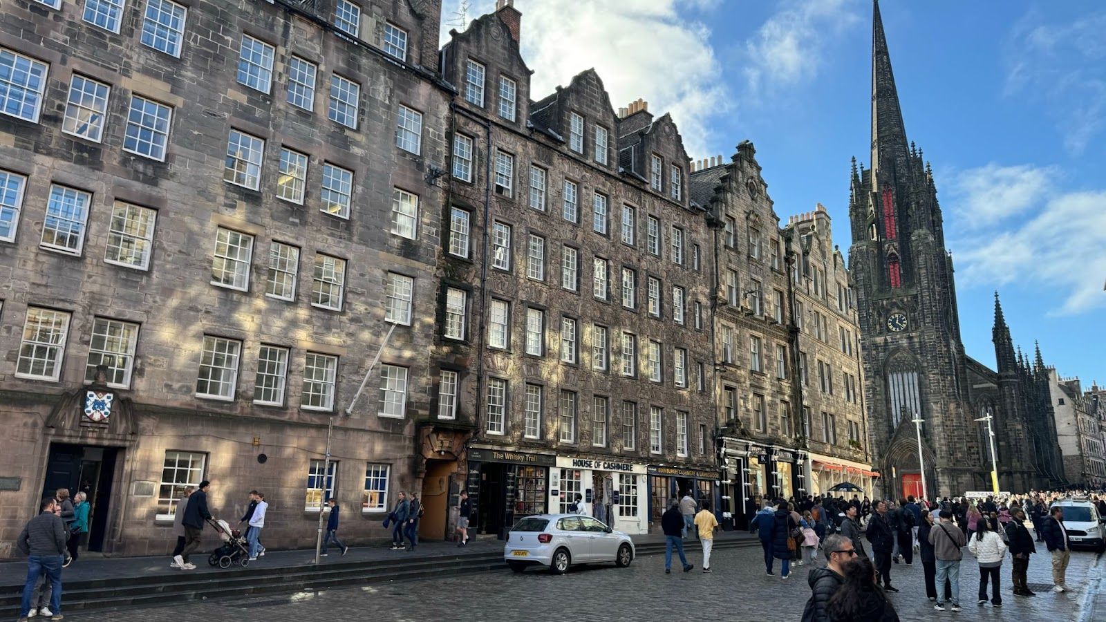 People walking on cobblestone next to large buildings with dozens of windows near The Royal Mile in Edinburgh.