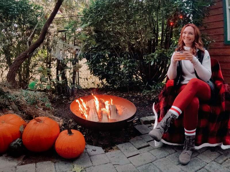Woman enjoying a fireside whisky next to an outdoor fire pit at a campsite.